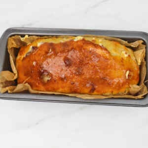 Freshly baked sourdough sandwich loaf in a baking pan lined with parchment paper.