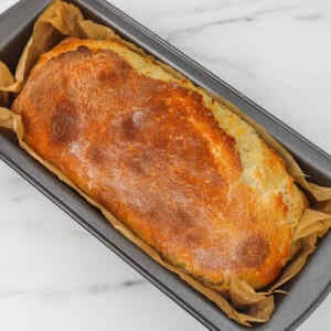Freshly baked sourdough sandwich loaf in a baking pan lined with parchment paper.