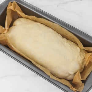A loaf of sourdough bread dough resting in a baking pan lined with parchment paper.