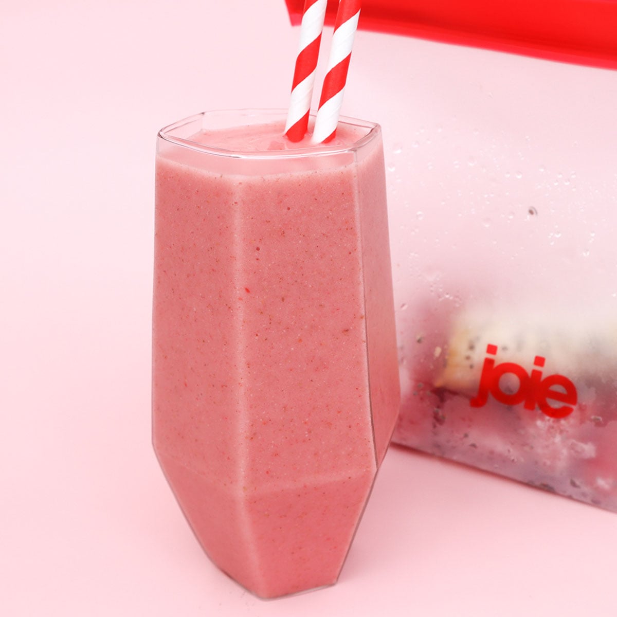 Strawberry and Banana Smoothie Freezer Meal Prep Packs A pink strawberry and banana smoothie in a glass with two striped straws.