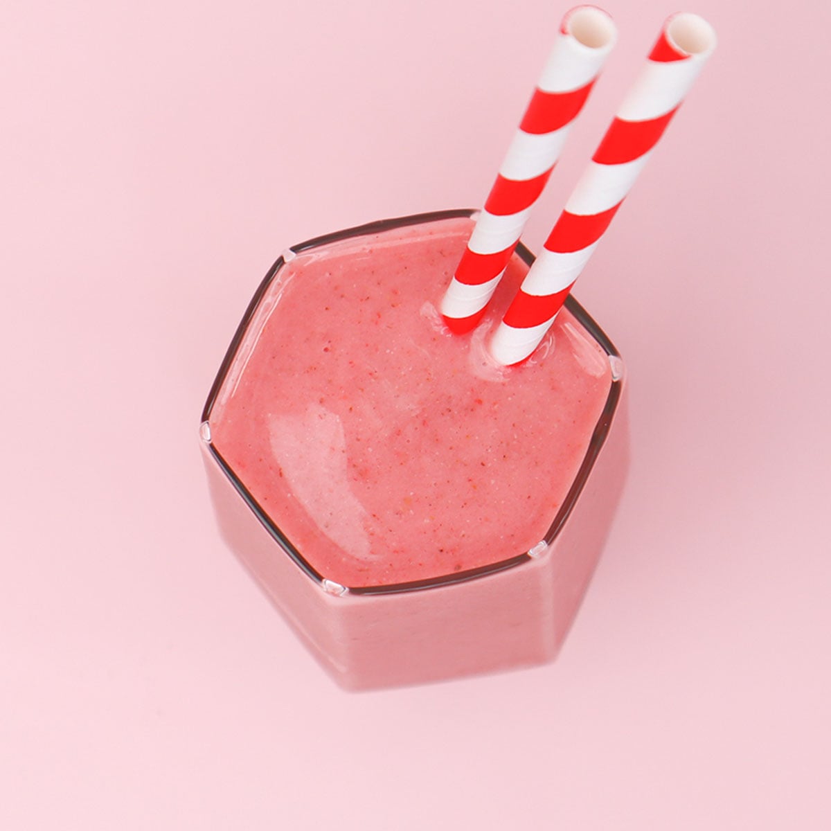 Strawberry and Banana Smoothie Freezer Meal Prep Packs A hexagonal glass filled with a pink strawberry and banana smoothie topped with two striped straws.