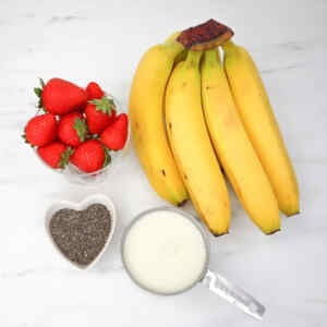 Fresh strawberries and bananas with chia seeds and milk for smoothie prep.