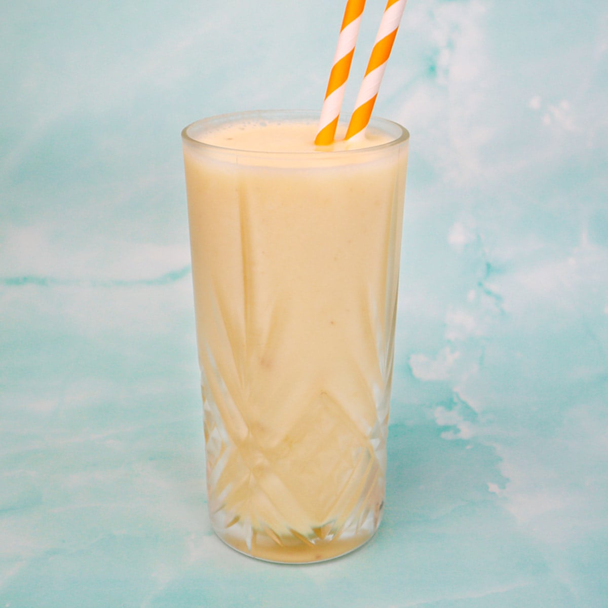 Tropical Smoothie Freezer Meal Prep Packs A creamy tropical smoothie in a tall glass with orange and white striped straws.