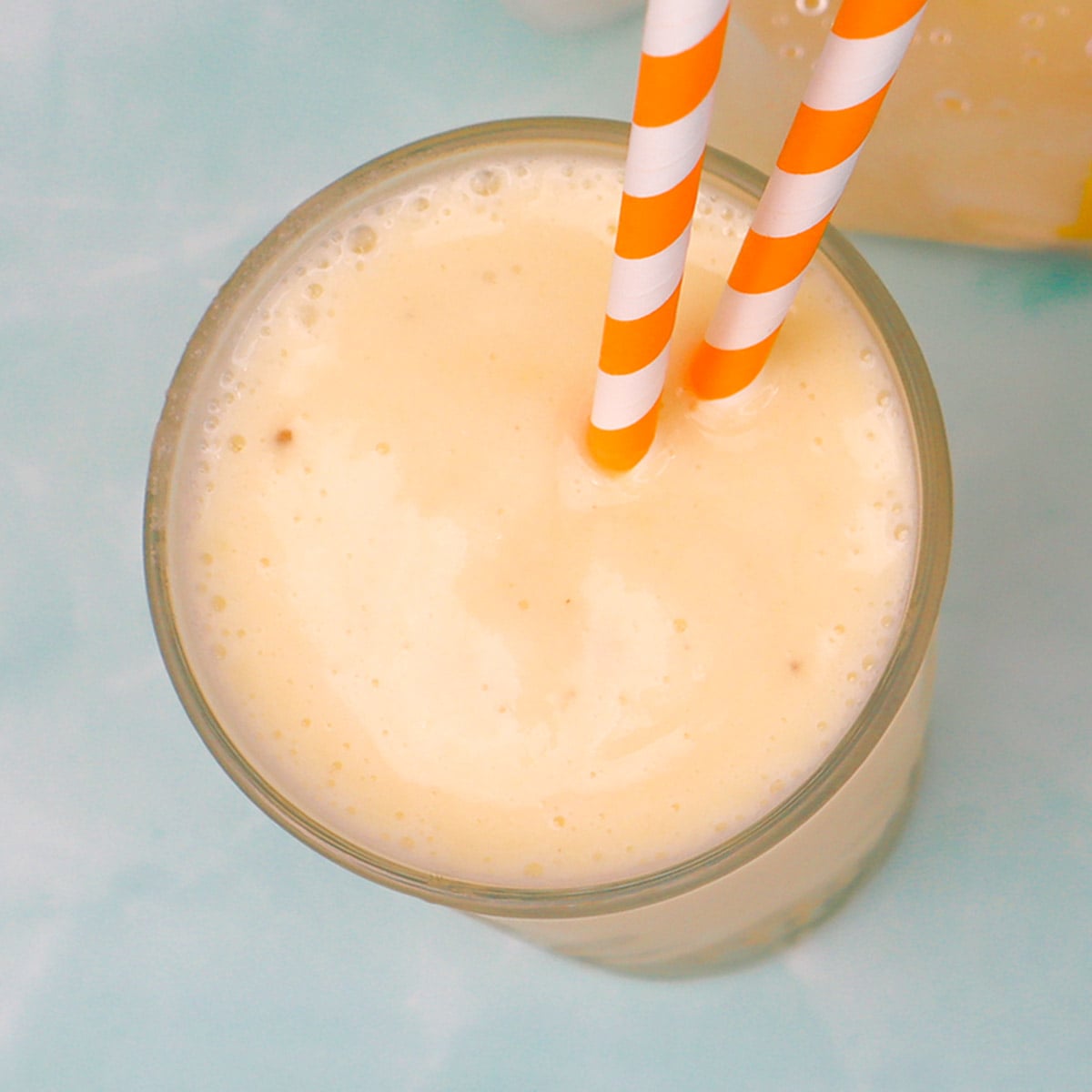 Tropical Smoothie Freezer Meal Prep Packs A creamy banana smoothie in a glass with orange and white striped straws.