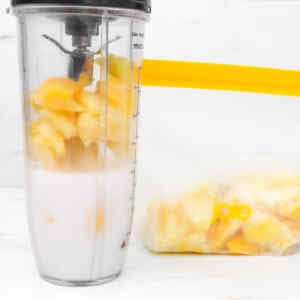 A blender filled with frozen fruit and milk, next to a bag of frozen fruit.