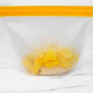 A clear bag filled with chopped tropical fruits, ready for smoothie meal prep.