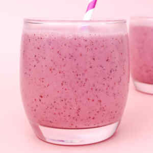 Primer plano de un batido de frutos rojos rosados en un vaso con pajita.