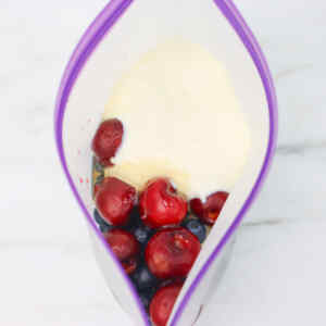 Un recipiente lleno de cerezas, arándanos y yogur para preparar un batido.