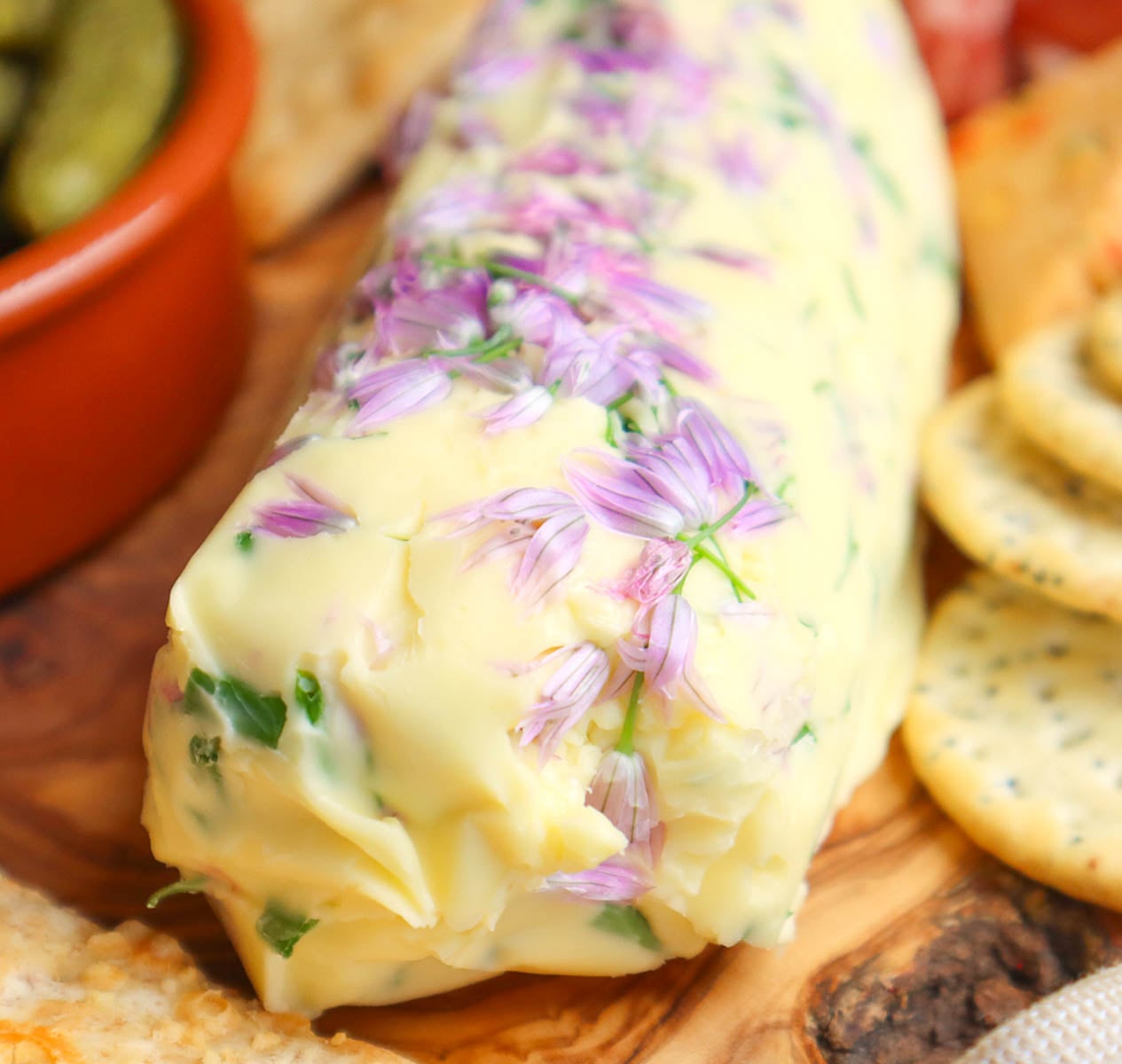 Hausgemachte Schnittlauchblütenbutter A log of homemade chive flower butter garnished with purple chive flowers, served with crackers.