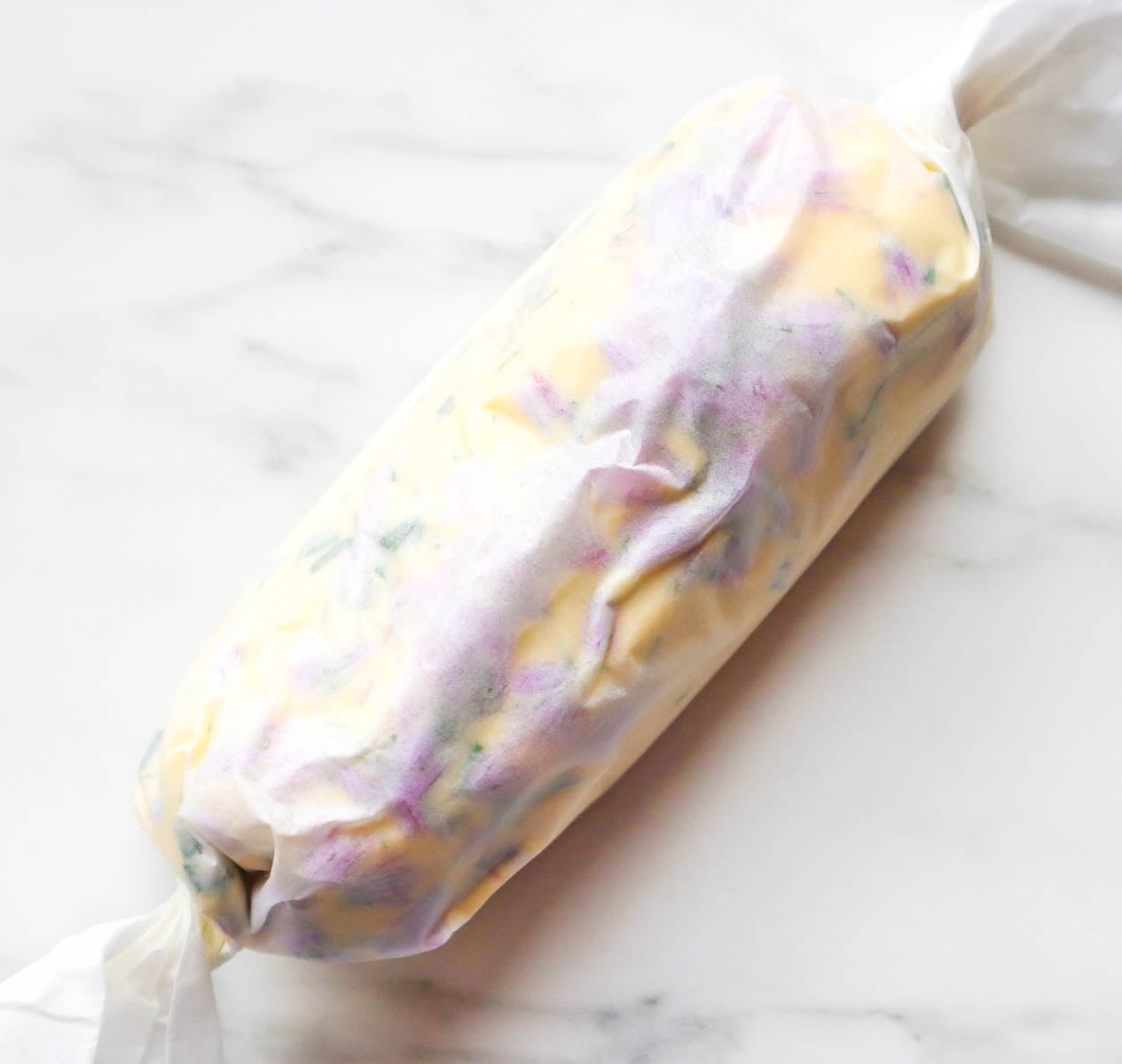Hausgemachte Schnittlauchblütenbutter A log of homemade chive flower butter wrapped in parchment paper.