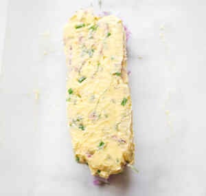 A log of homemade chive flower butter spread on parchment paper.
