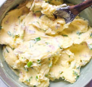 Creamy homemade chive flower butter mixed with fresh herbs in a bowl.