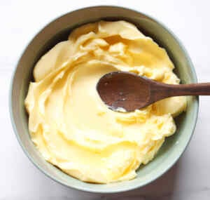Creamy homemade chive flower butter in a bowl with a wooden spoon.
