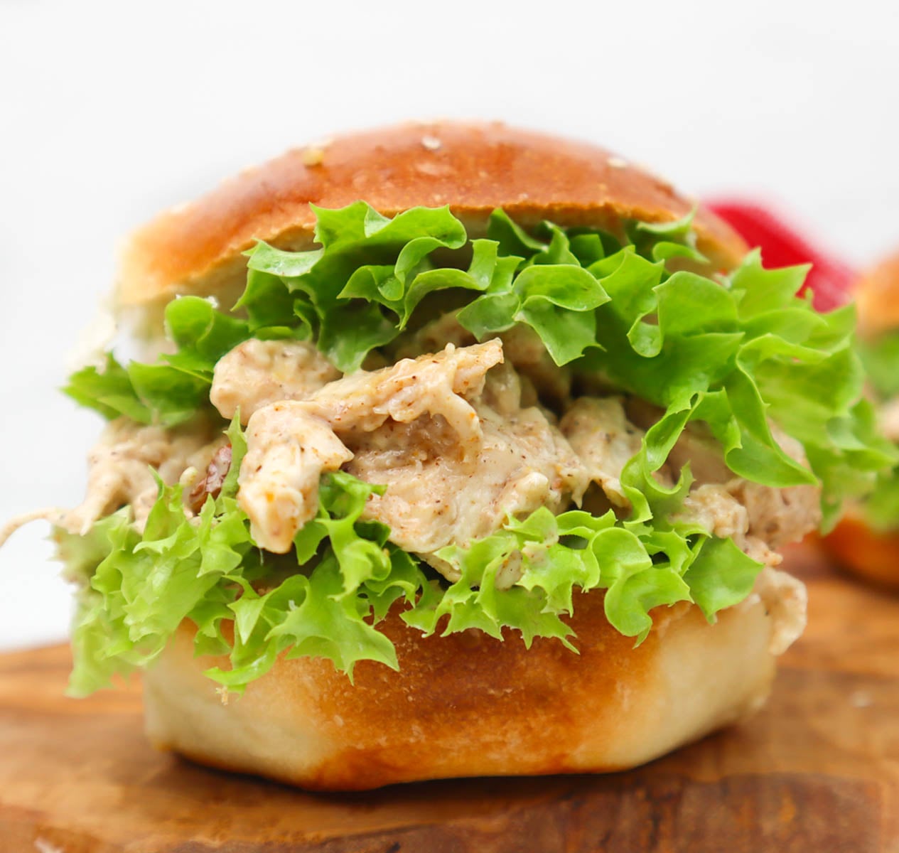 Coronation Chicken Sandwich A close-up of a coronation chicken sandwich with lettuce on a wooden board.