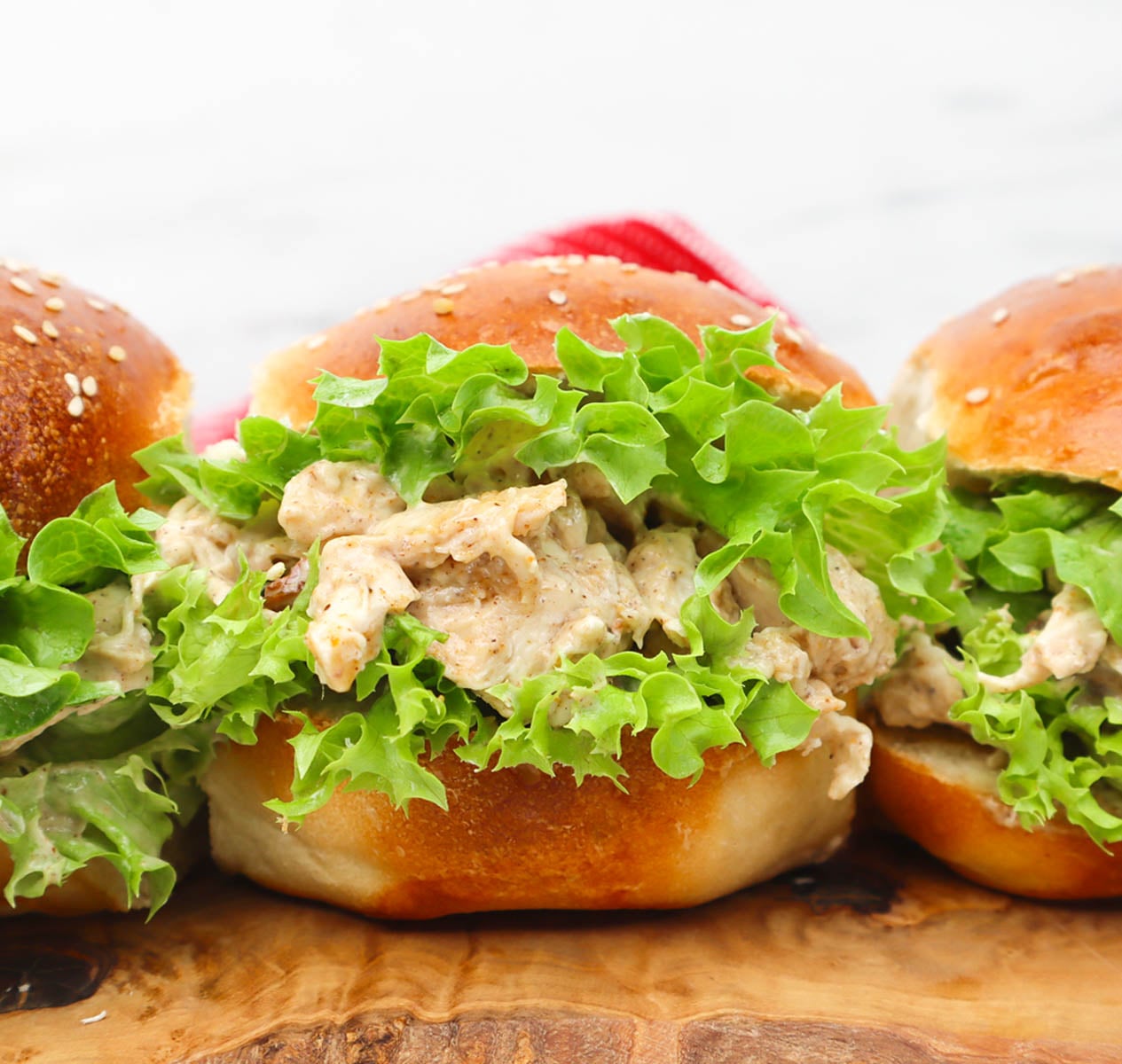 Coronation Chicken Sandwich Drei Coronation Chicken Sandwiches mit Salat auf einem Holzbrett.