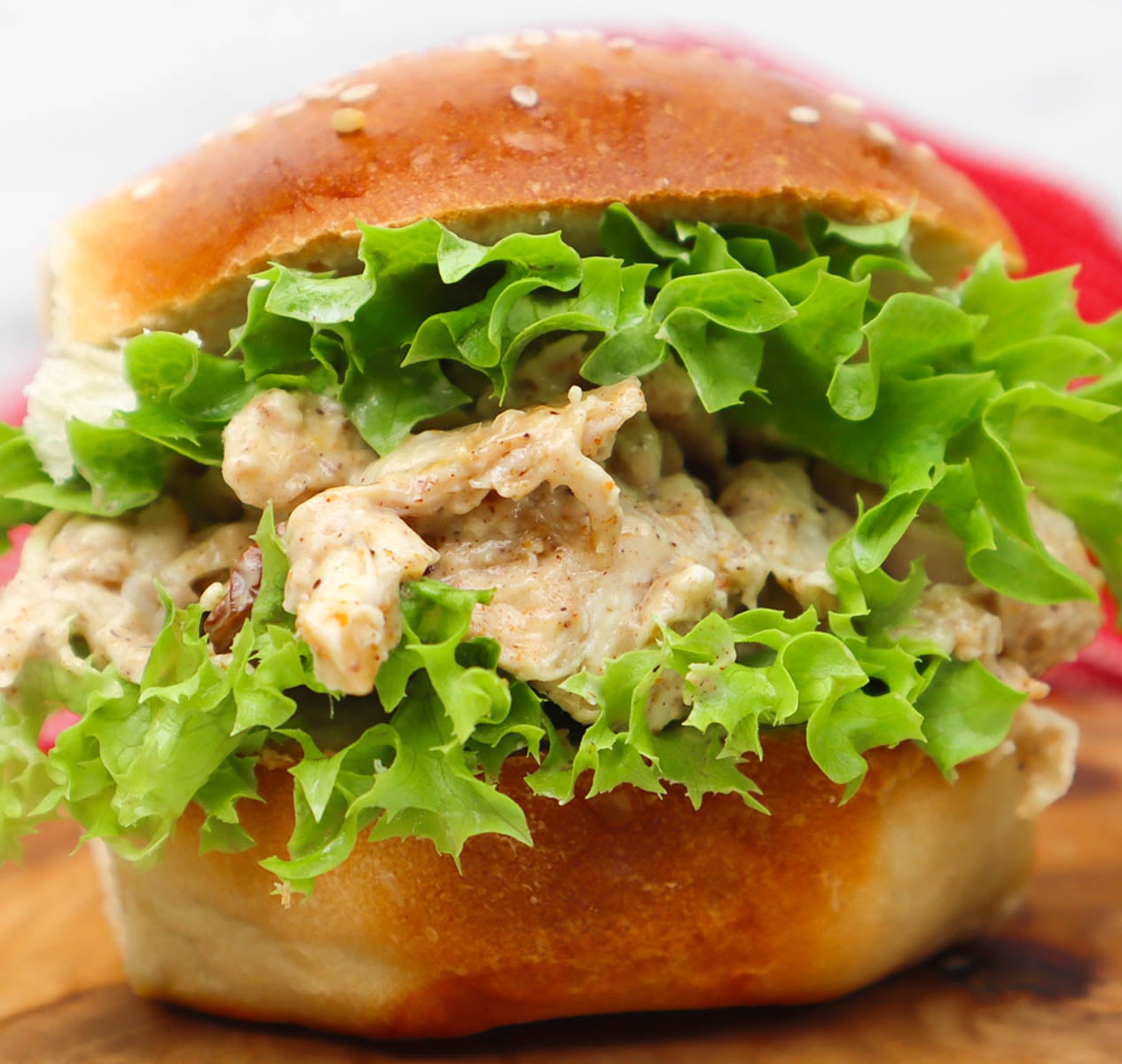 Coronation Chicken Sandwich A close-up of a coronation chicken sandwich with lettuce on a sesame seed bun.