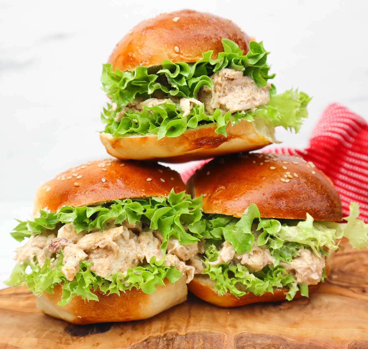 Coronation Chicken Sandwich Drei Coronation Chicken Sandwiches mit Salat auf einem Holzbrett.