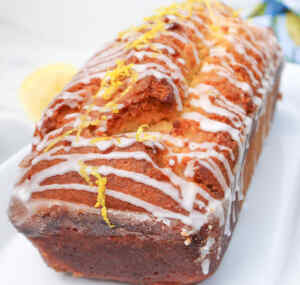 A close-up of a lemon drizzle cake topped with icing and lemon zest.