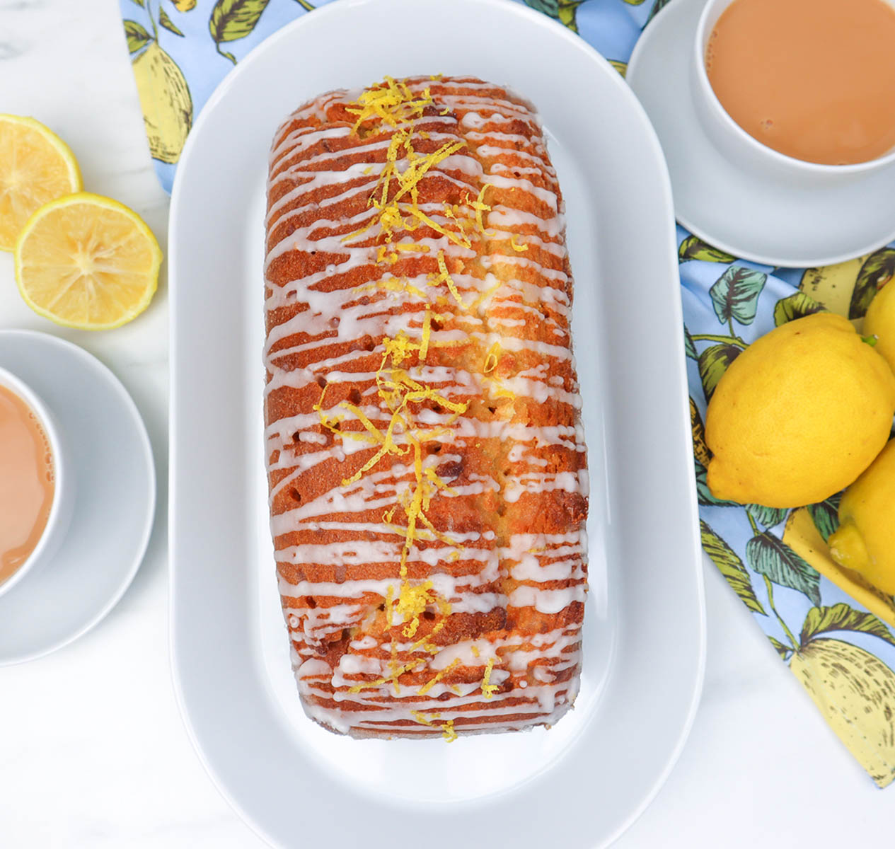 Lemon Drizzle Cake A lemon drizzle cake topped with icing and lemon zest, served with tea and fresh lemons.