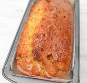 A freshly baked lemon drizzle cake in a gray loaf pan, glistening with a sweet glaze.