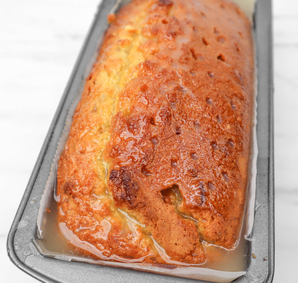 Lemon Drizzle Cake A freshly baked lemon drizzle cake in a gray loaf pan, glistening with a sweet glaze.