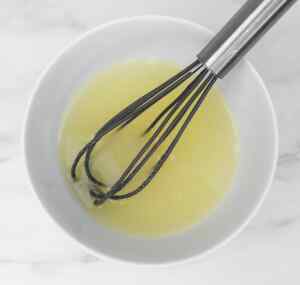 A whisk in a bowl of lemon mixture, ready for making lemon drizzle cake.