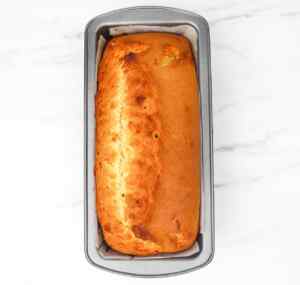 A freshly baked lemon drizzle cake in a loaf pan on a marble surface.