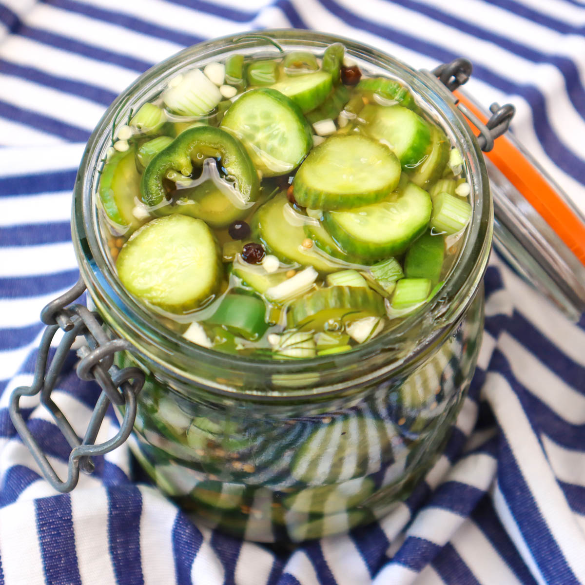 Quick Pickled Cucumbers A jar filled with sliced cucumbers in a pickling brine, resting on a striped cloth.