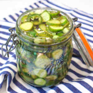 A jar filled with quick pickled cucumbers resting on a striped cloth.