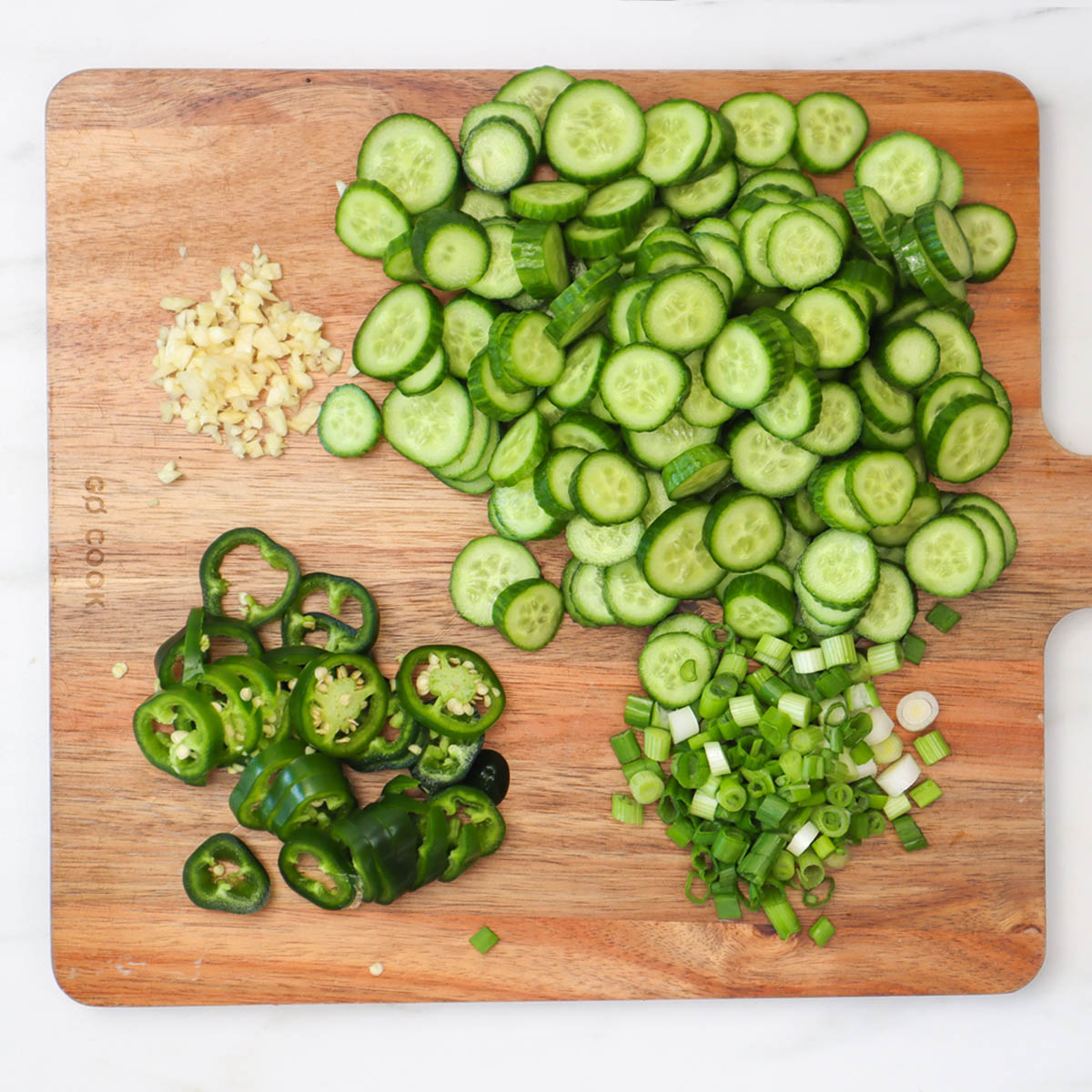 Quick Pickled Cucumbers Sliced cucumbers, jalapeños, and chopped green onions on a wooden cutting board.