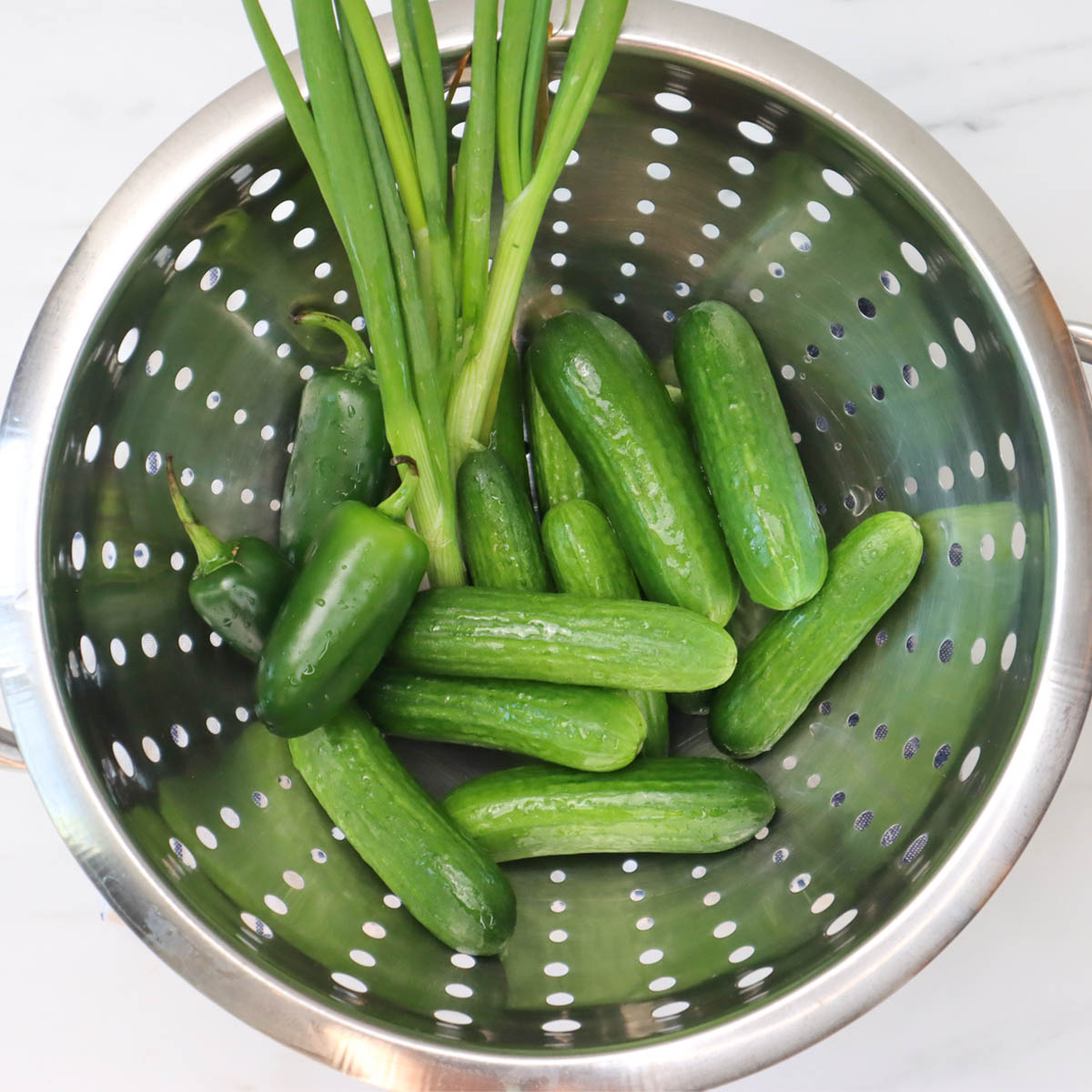 Quick Pickled Cucumbers Fresh cucumbers and green onions in a colander, ready for pickling.