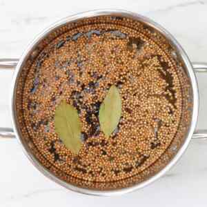 A pot filled with mustard and coriander seeds and bay leaves in a brine solution.