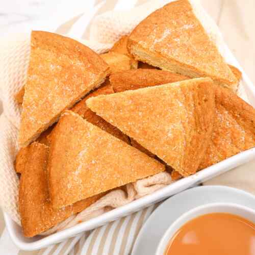 A plate of triangular Scottish shortbread cookies with a cup of tea beside it.
