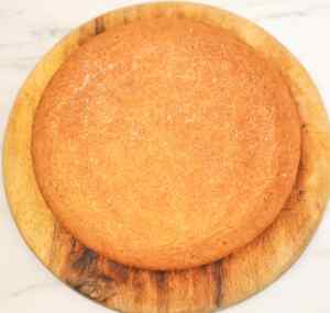 A round Scottish shortbread on a wooden board, lightly sprinkled with sugar.