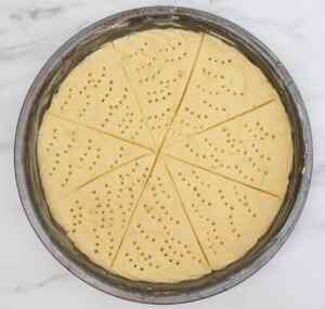 A round pan of unbaked Scottish shortbread dough, scored into wedges with holes on top.