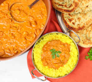A bowl of slow cooker chicken tikka curry served over yellow rice, with naan bread on the side.