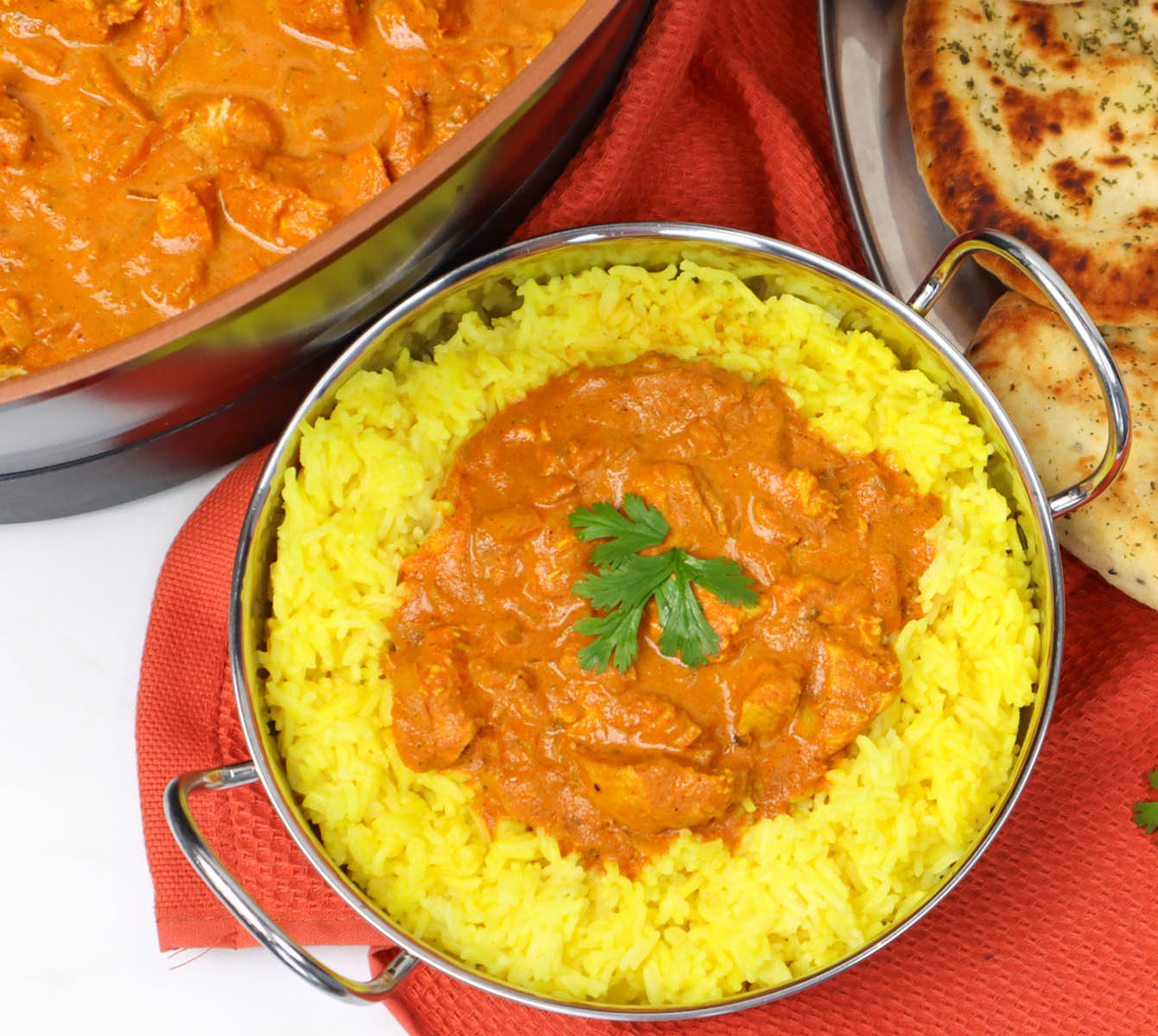 Slow Cooker Chicken Tikka Curry A bowl of slow cooker chicken tikka curry served with yellow rice and naan bread on a red cloth.