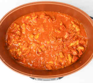 A slow cooker filled with chicken tikka curry in a rich, red sauce.