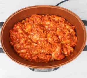 A slow cooker filled with chicken tikka curry, featuring a rich, red sauce and tender chicken pieces.