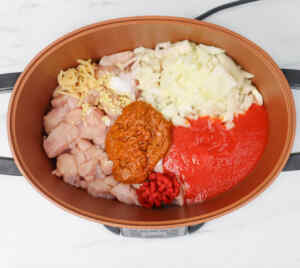 Ingredients for slow cooker chicken tikka curry, including chicken, onions, and sauces in a pot.