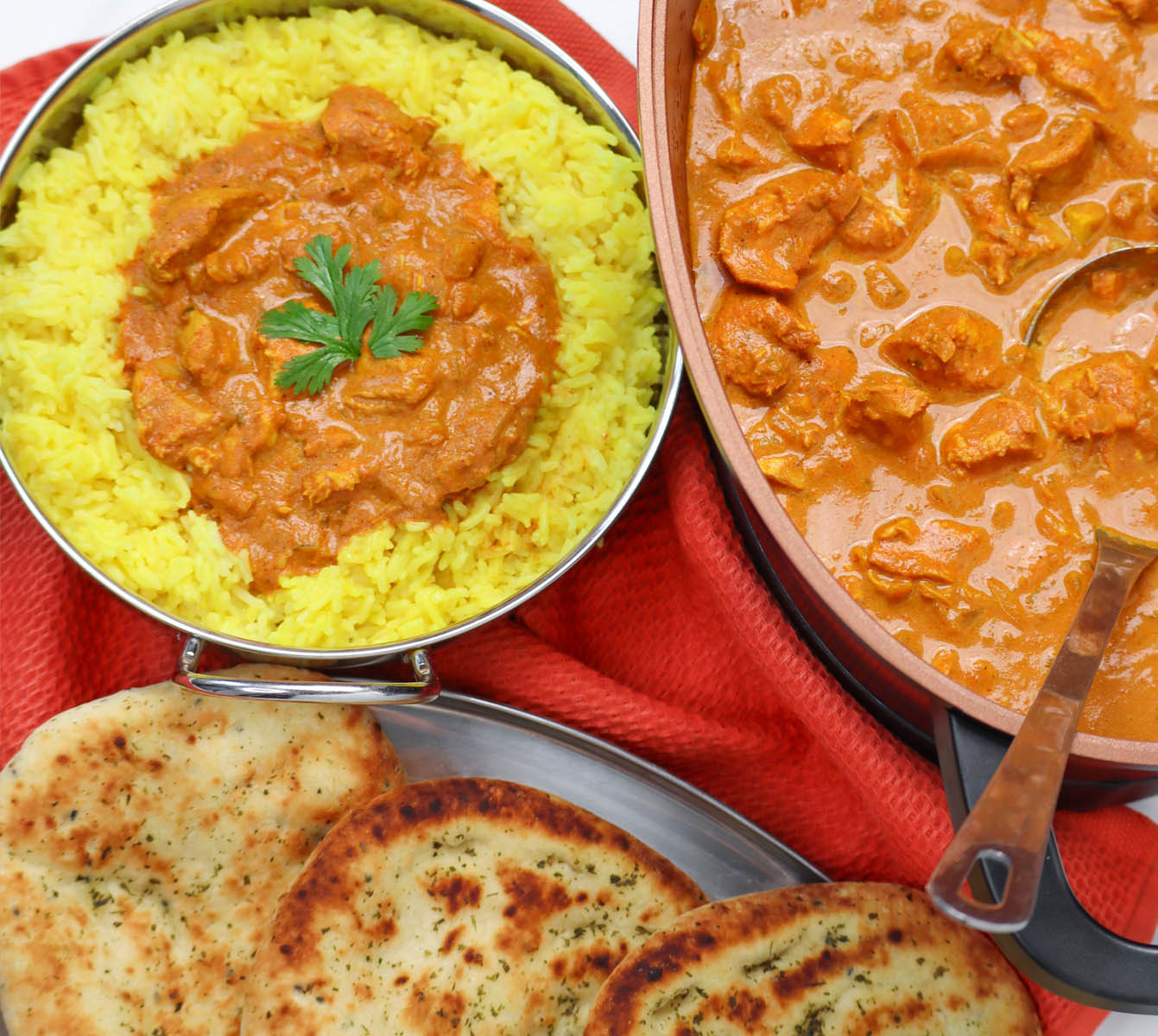 Slow Cooker Chicken Tikka Curry A bowl of chicken tikka curry served with yellow rice and naan bread on a red cloth.