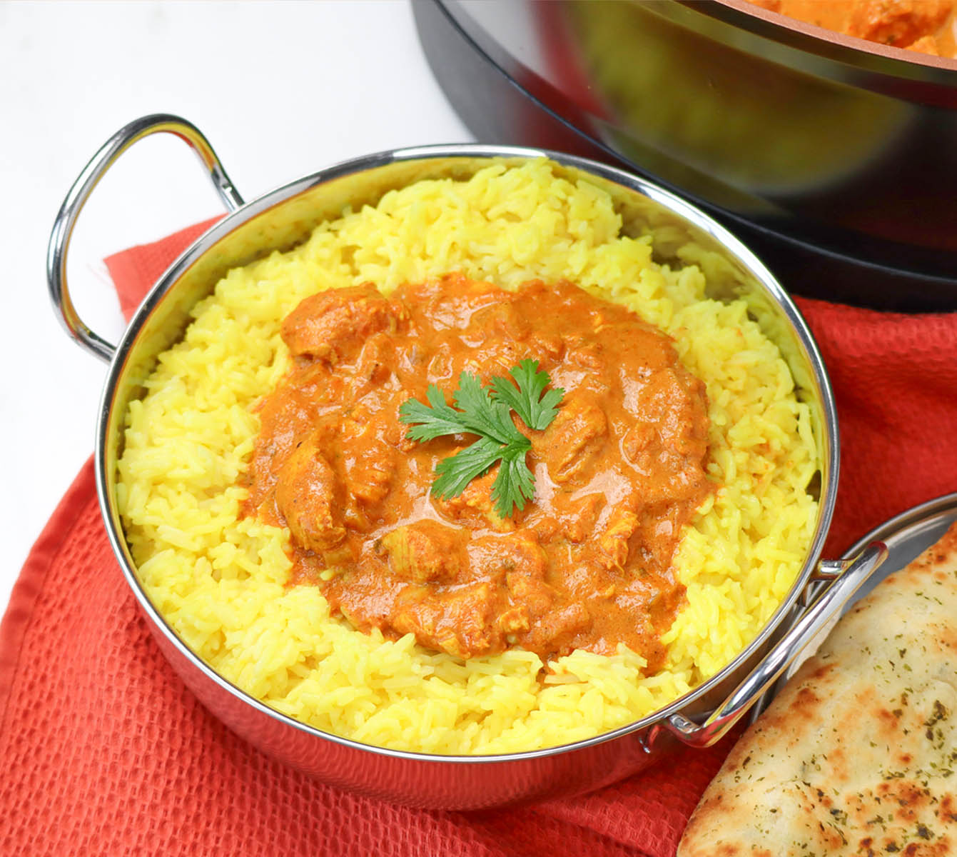 Slow Cooker Chicken Tikka Curry A bowl of chicken tikka curry served over yellow rice, garnished with cilantro, next to naan bread.