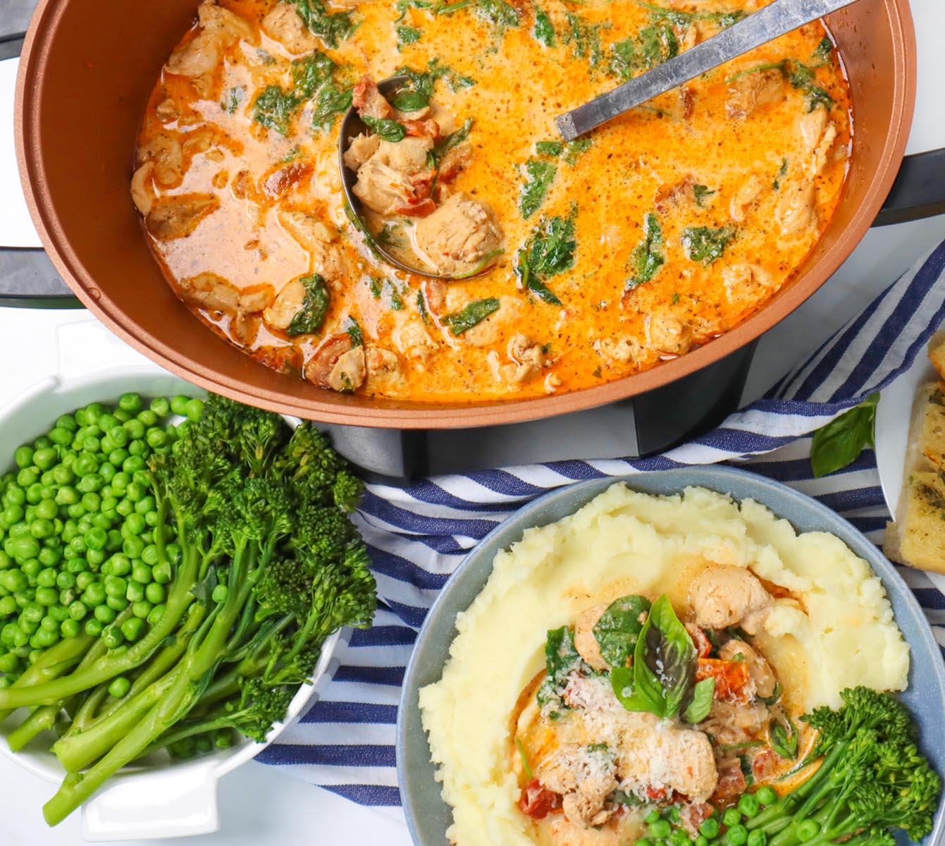 Slow Cooker Marry Me Chicken A bowl of creamy chicken with spinach and tomatoes served over mashed potatoes, alongside green peas and broccoli.