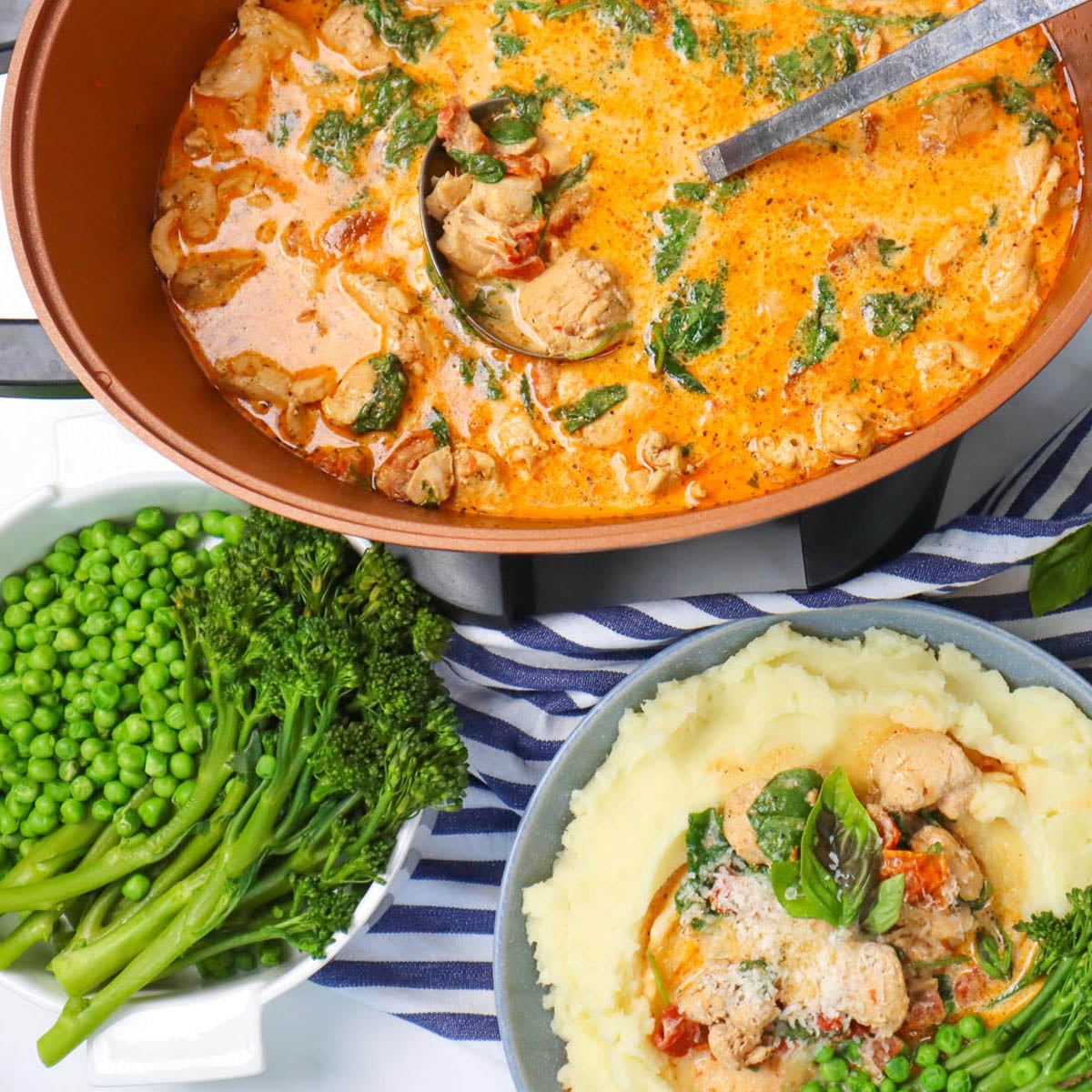 A bowl of creamy slow cooker chicken with spinach and tomatoes, served with mashed potatoes and green vegetables.