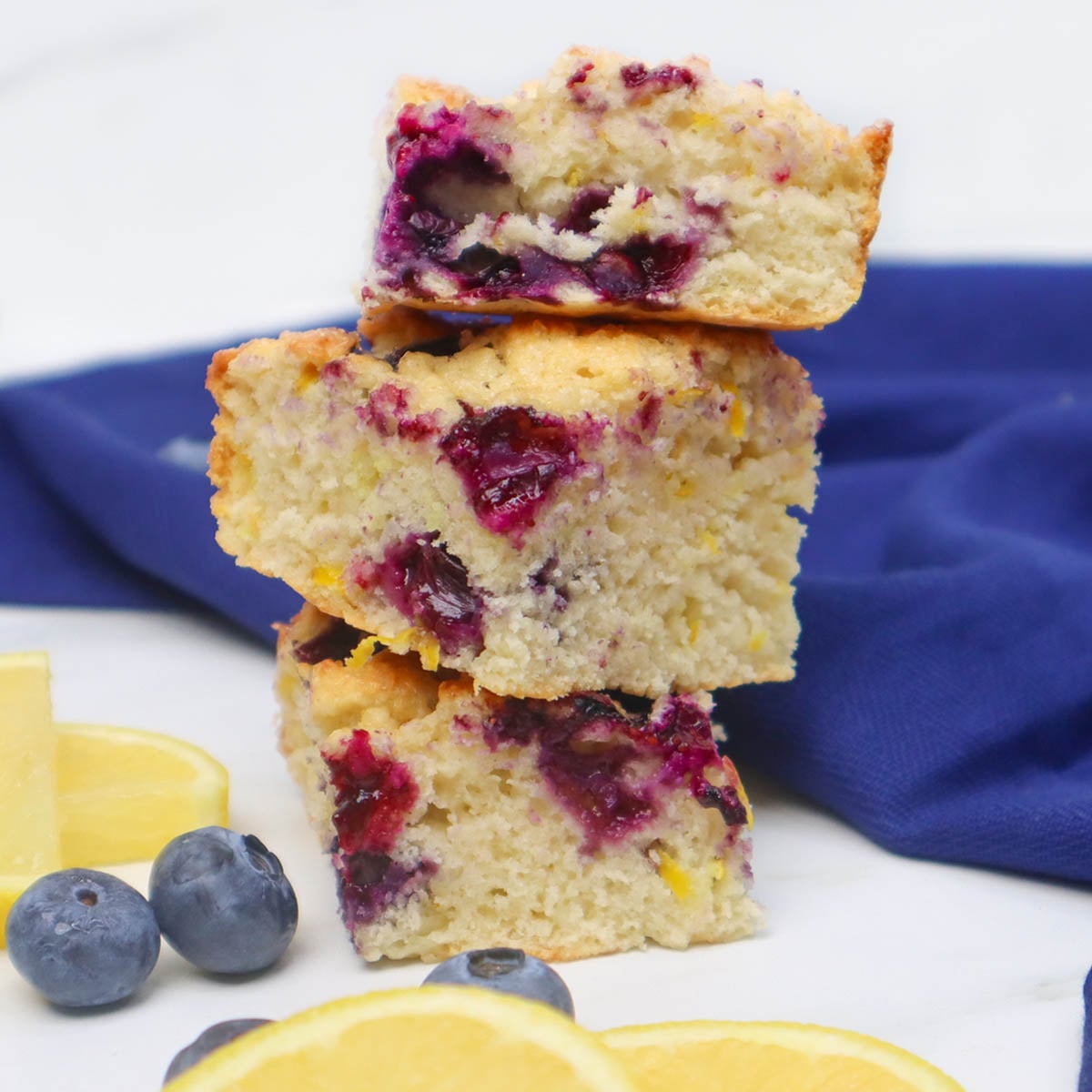 American Style Blueberry Biscuits Three stacked blueberry biscuits with lemon slices and blueberries on a marble surface.