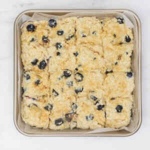 A tray of freshly baked American-style blueberry biscuits cut into squares.