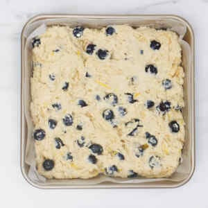 A square baking dish filled with blueberry biscuit dough, dotted with fresh blueberries.