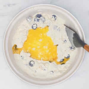 A bowl with flour, blueberries, and an egg yolk being mixed together.