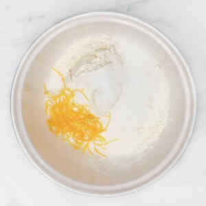 A bowl containing flour, sugar, and lemon zest, ready for baking blueberry biscuits.