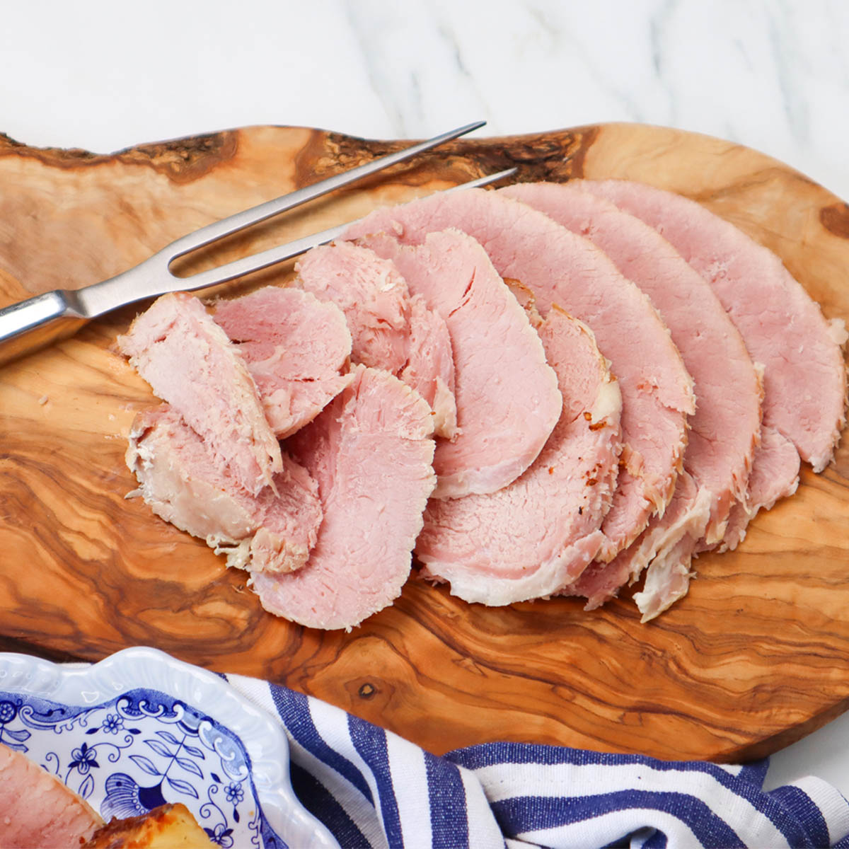 Slow Cooker Ham Sliced slow cooker ham arranged on a wooden board with a carving fork.